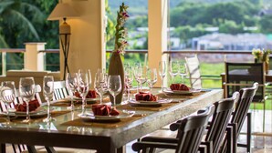 A dining table set with wine glasses, plates, and napkins, with a view of greenery and buildings in the background. - Viola Pool Villa (Rawai)