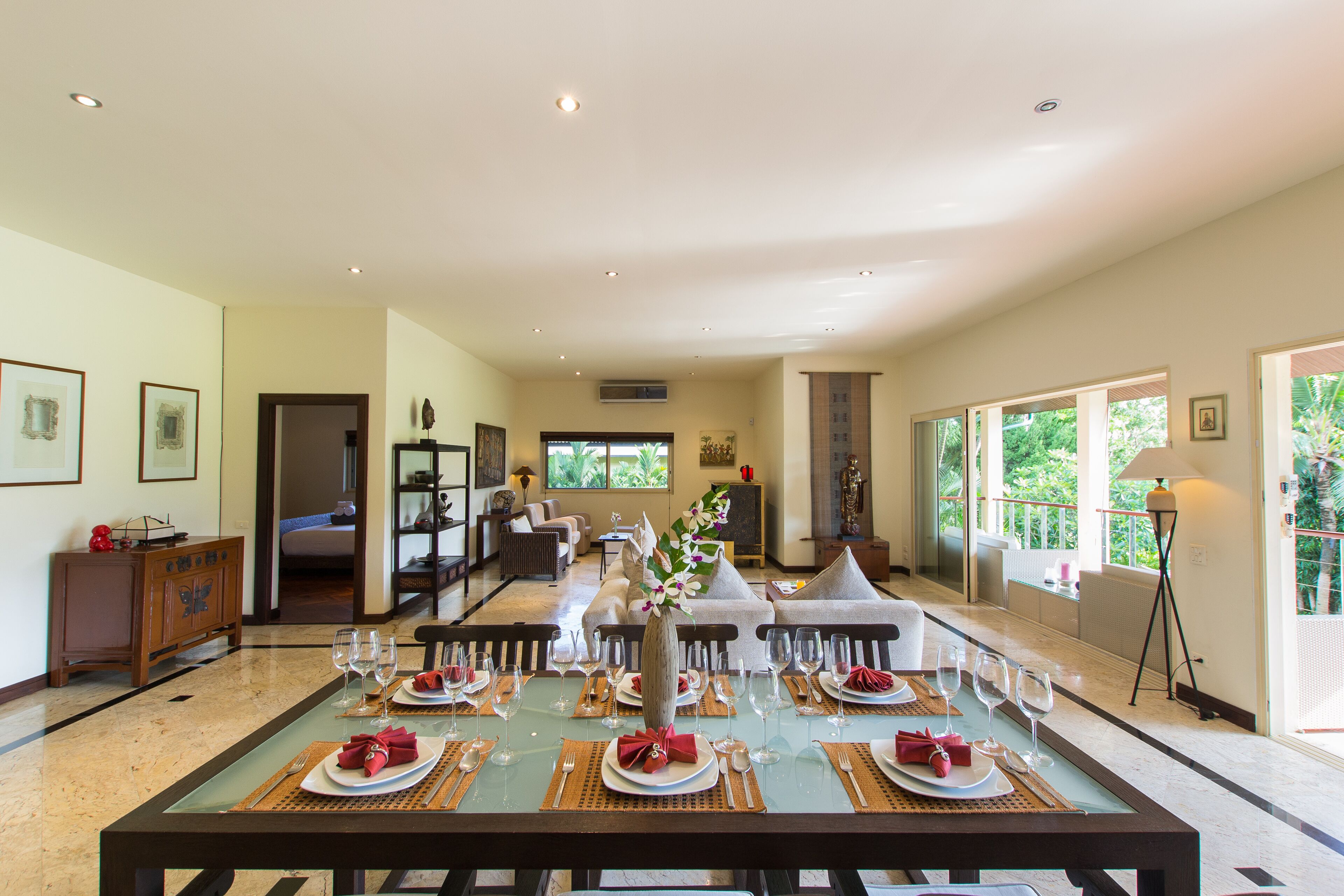 A spacious dining area with a long table set for a meal, a sofa, and a view of the outdoors.