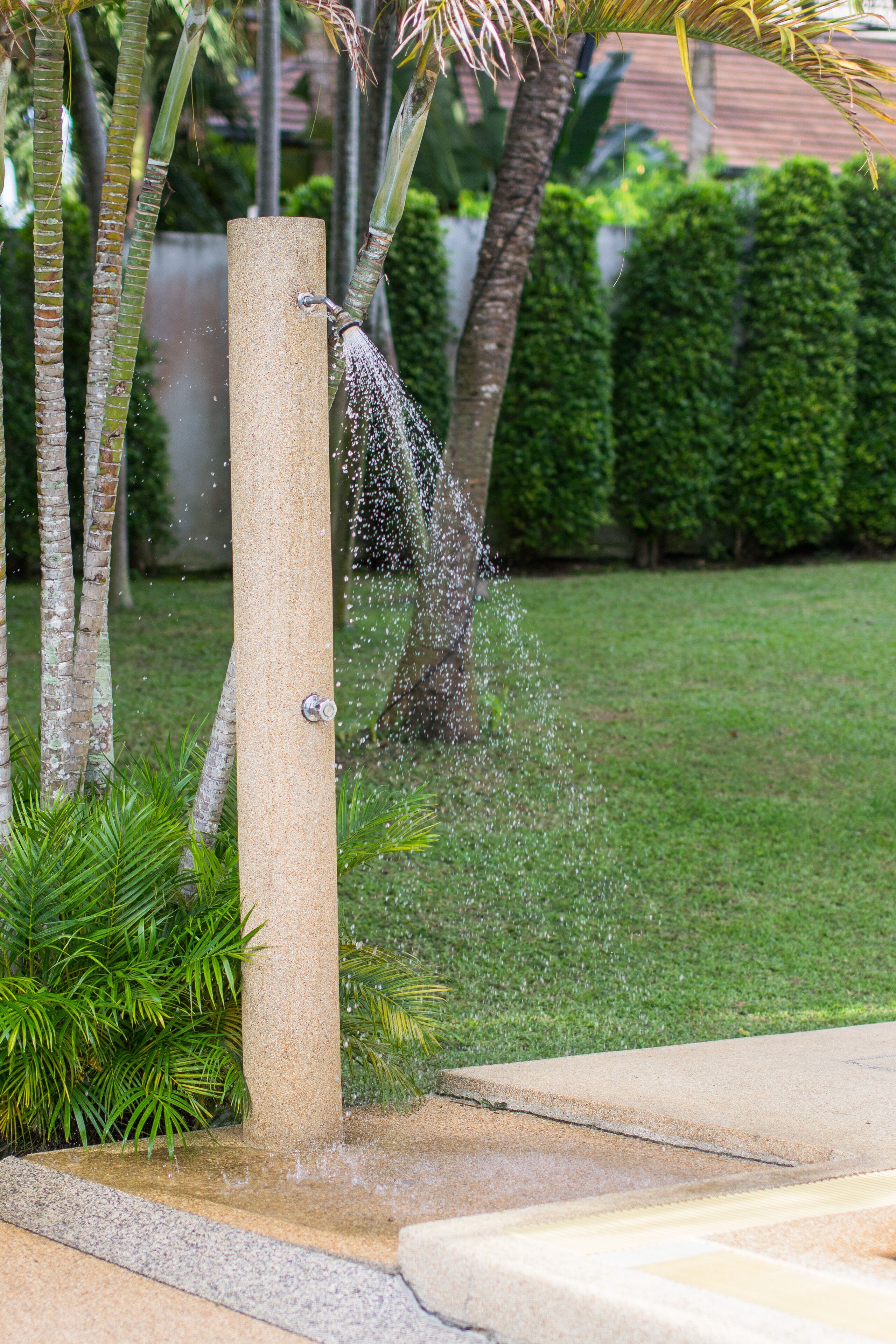 Un pilar de concreto con un caño de agua, rodeado de follaje y palmeras.