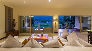 A spacious living room with a large sofa, a coffee table, and a view of a lush garden through large sliding glass doors. - Viola Pool Villa (Rawai)