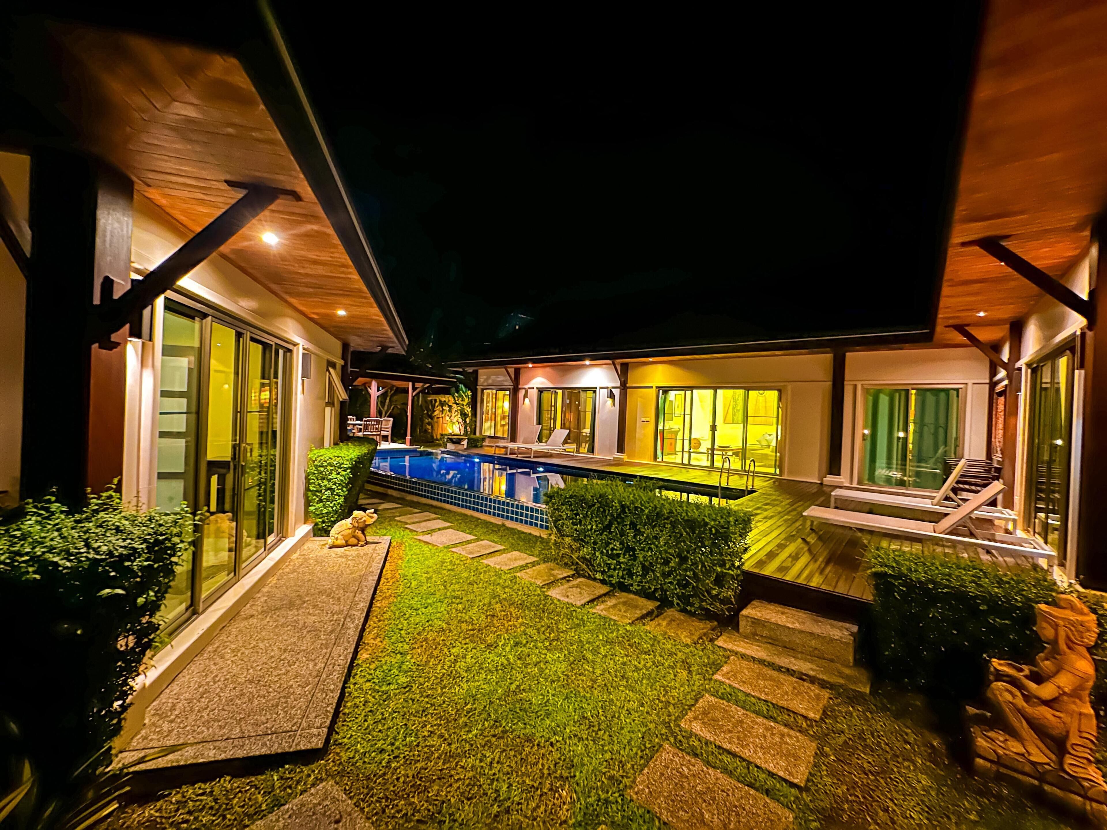 Una casa moderna con piscina, mobiliario exterior y un patio bien iluminado.