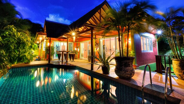 Un hotel con piscina, mobiliario exterior y plantas tropicales.