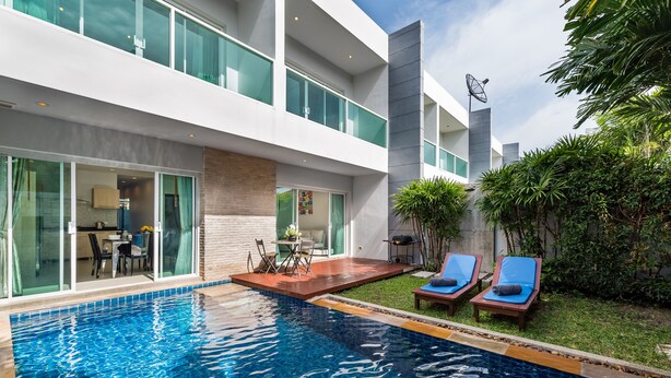 Un espace piscine moderne offrant une vue dégagée sur la piscine, des chaises longues et un patio avec une table et des chaises.