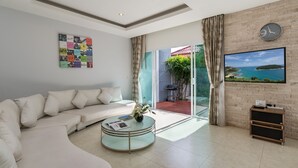 Un salon moderne avec un canapé blanc, une table basse en verre, un téléviseur à écran plat et une grande fenêtre donnant sur un paysage côtier.
