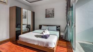 Une chambre d’hôtel moderne avec un lit en bois, un grand miroir, une œuvre d’art représentant un paysage urbain et une porte-fenêtre coulissante.