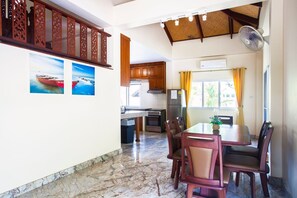 A spacious dining area with a marble floor, wooden dining table, and chairs. There is a kitchen area with wooden cabinets and a refrigerator. - Twin Palm Pool Villa (Rawai)