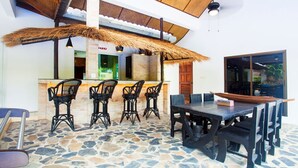 Un área de bar con techo de paja, suelo de piedra y sillas de metal negro.