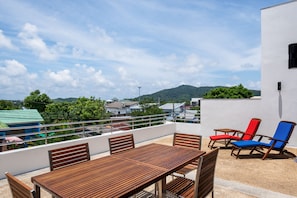 A wooden table and chairs on a balcony with a view of a mountain and buildings. - Sky Pool Villa (Rawai)