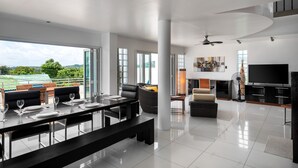 A modern living room with a dining area, large windows, a flat-screen TV, and a ceiling fan. - Sky Pool Villa (Rawai)