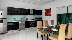 A modern kitchen with black cabinets, a dishwasher, and a dining area with a glass table and chairs. - Crystal Pool Villa (Rawai)