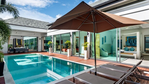 A modern outdoor pool area with lounge chairs and a large umbrella, surrounded by glass doors and potted plants. - Crystal Pool Villa (Rawai)