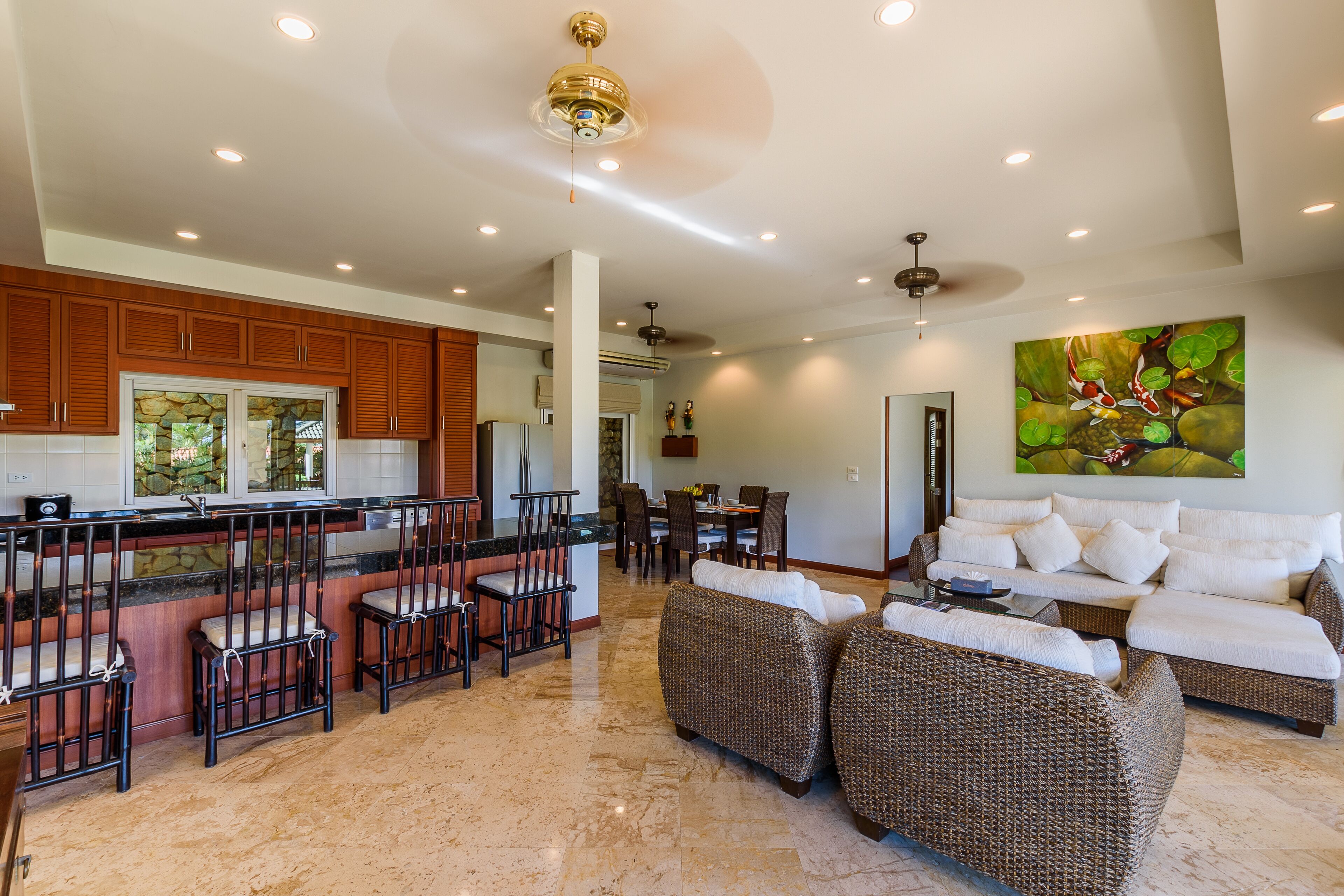 A spacious living area with a dining table, wicker sofas, and a kitchen with wooden cabinets and a stone backsplash.