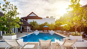 A swimming pool with lounge chairs and umbrellas, surrounded by potted plants and a building with a tiled roof. - The Sands 2 bedroom apartment (Rawai)
