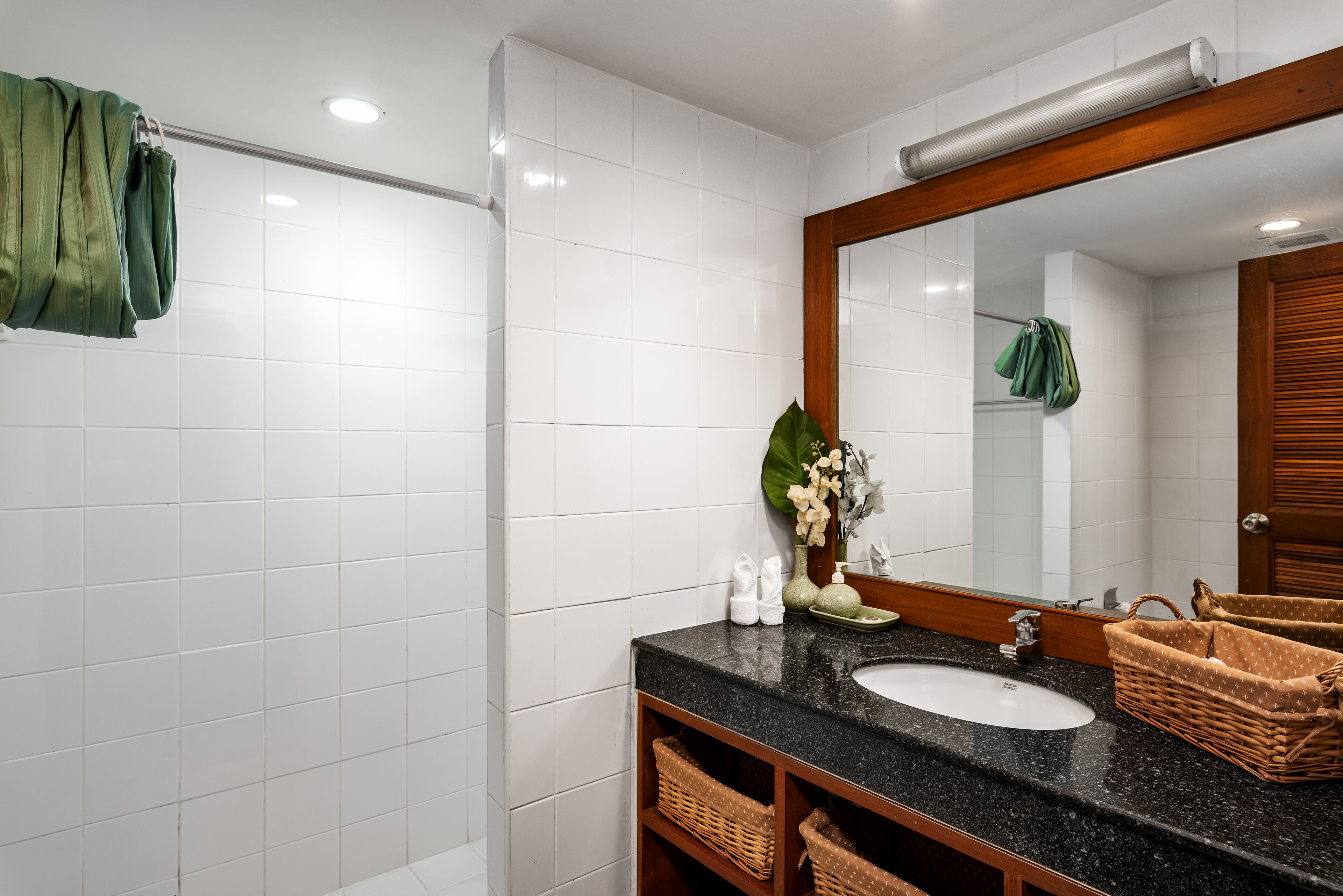 A bathroom with white tiles, a black sink, a mirror, and wicker baskets.