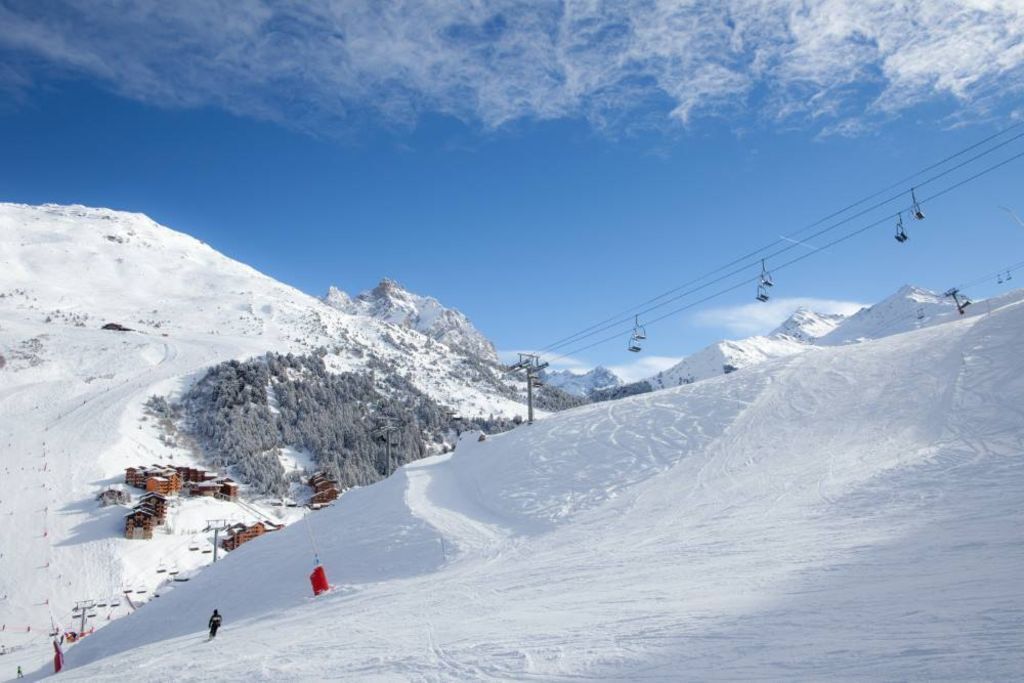 A snow-covered ski slope with ski lifts and a mountain backdrop.