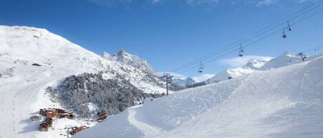 A snow-covered ski slope with ski lifts and a mountain backdrop.