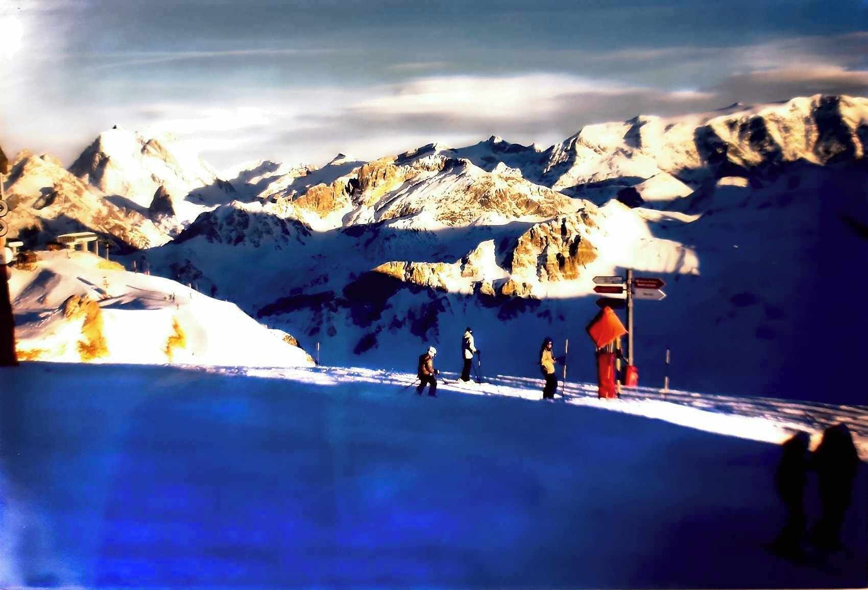 Schneegebirgslanschaft mit Skipiste, einem roten Wegweiser und einigen Skifahrern.