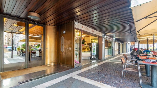 A modern building with a wooden ceiling, a café area with outdoor seating, and a visible entrance.