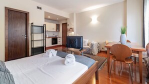 A hotel room with a bed, a desk, a television, a dining table, and a kitchenette.