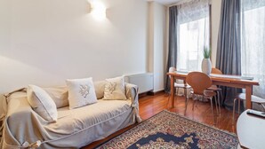 A living room with a sofa, a dining table, chairs, a rug, and a window with curtains.