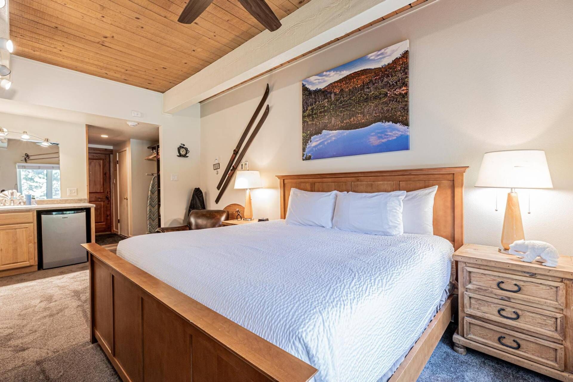 Une chambre à coucher avec un lit en bois, des lampes de chevet, une table de chevet en bois, un tableau représentant un paysage montagneux et un plafond en bois.