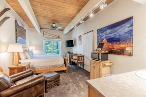 A bedroom with a bed, a desk, a television, and a painting on the wall.