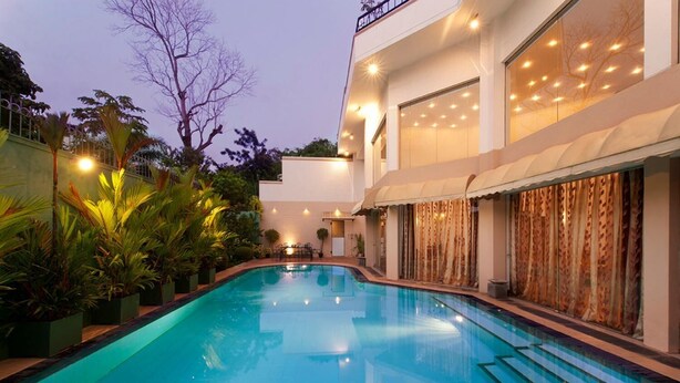 A swimming pool with a curved design, surrounded by lush greenery and modern buildings. - Villa 53 (Battaramulla)