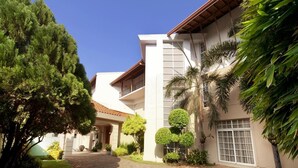A modern building with a paved driveway, surrounded by well-maintained greenery and palm trees. - Villa 53 (Battaramulla)