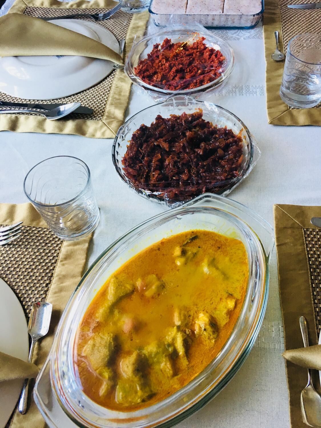 Una mesa de comedor con un tazón de vidrio con curry, un tazón de chutney rojo y un vaso de agua.