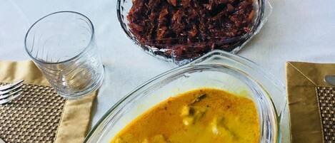 Una mesa de comedor con un tazón de vidrio con curry, un tazón de chutney rojo y un vaso de agua.