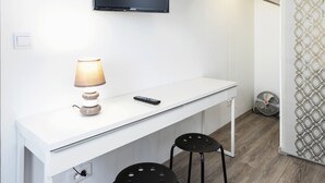A compact room with a white desk, a mounted TV, a lamp, and two stools. - STUDIO ZEN Gare St Jean (Bordeaux)