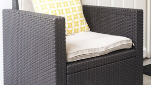 A wicker chair with a cushion and a patterned pillow, placed in front of a white door. - STUDIO ZEN Gare St Jean (Bordeaux)