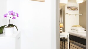 A modern hotel room with a wooden floor, a white desk with a potted orchid, a bed with white bedding, and a wall-mounted artwork. - STUDIO ZEN Gare St Jean (Bordeaux)