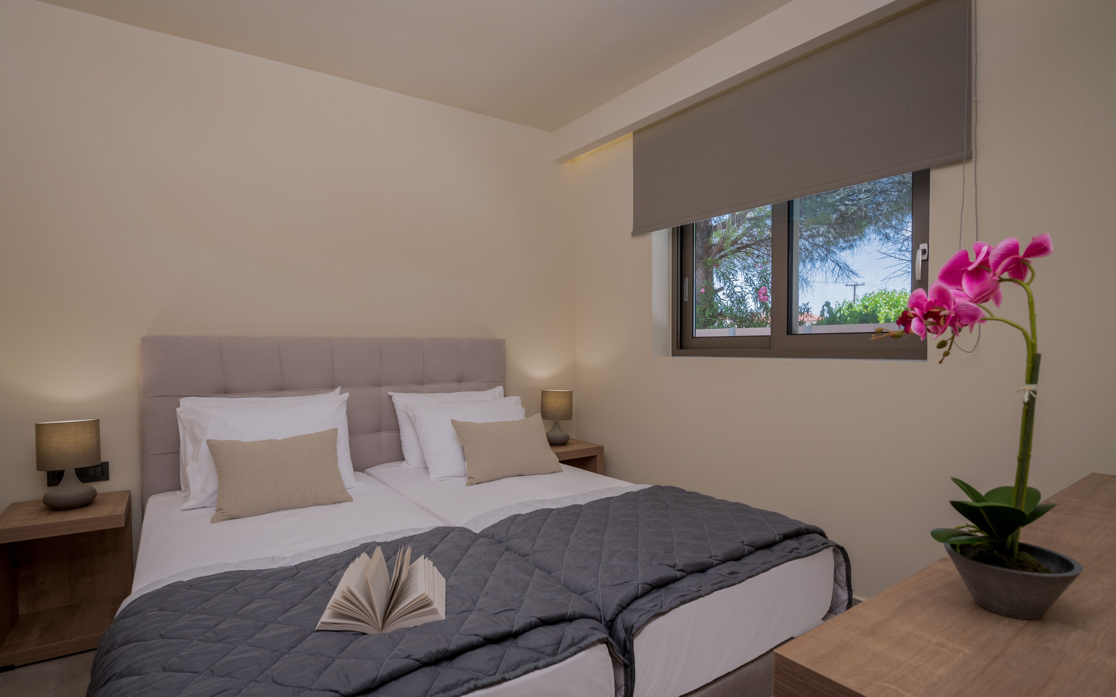 Une chambre à coucher avec un lit, deux tables de chevet, une fenêtre donnant sur un beau paysage et une plante en pot.