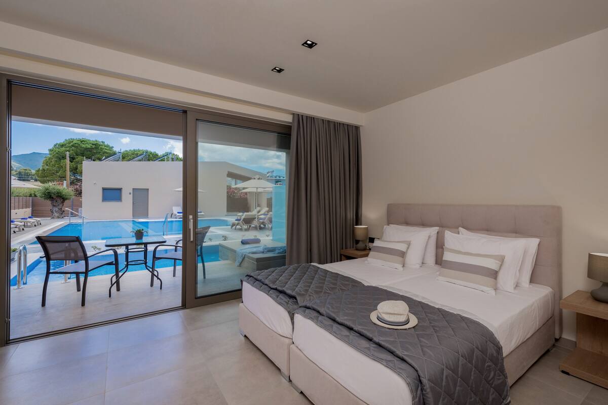 Una camera d'albergo moderna con un letto grande, vista su una piscina all'aperto e un balcone con posti a sedere.