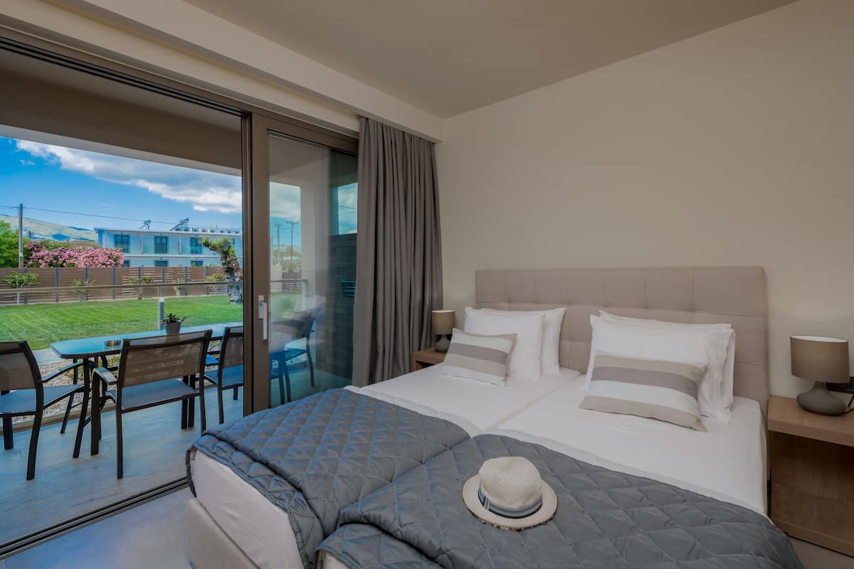 Una camera d'albergo con un letto grande, un'area pranzo con tavolo e sedie, e vista su un edificio e un giardino.