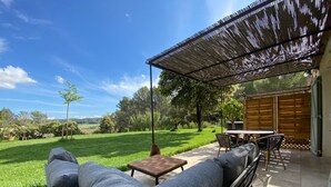 A patio with a sofa, table, and chairs under a pergola, overlooking a grassy area with trees and a distant view. - B&B Mas Lou Felibrige (Venelles)
