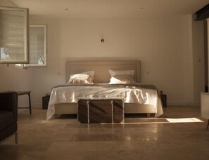 A modern bedroom with a large bed, a bedside table, a chair, and a large window.