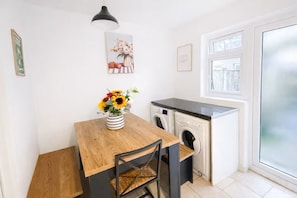 Eine kleine Küche mit Holztisch, Blumenvase, Waschmaschine und Fenster mit Aussicht.