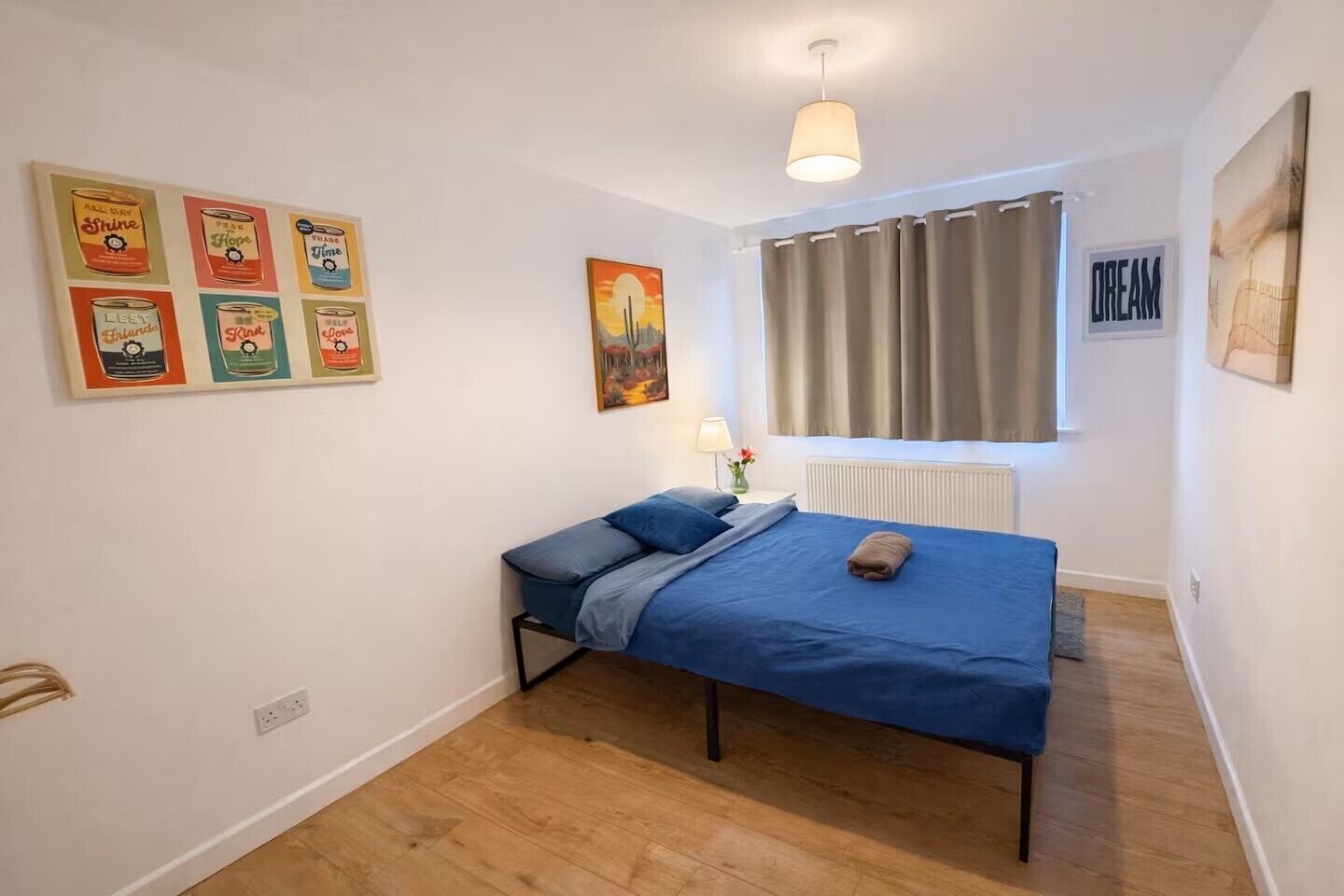 A bedroom with a bed, a window with curtains, a radiator, and wall art.