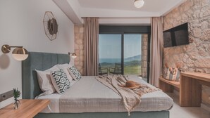A bedroom with a large bed, a stone wall, a TV, and a view of the outdoors.