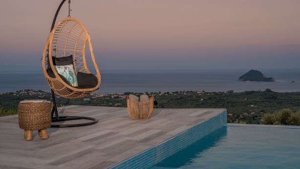 A hanging chair by a pool with a view of the sea and a distant island.