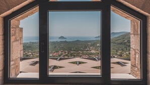 A view through a stone-framed window, overlooking a coastal town with houses and the sea.