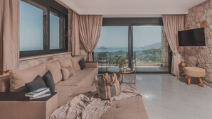 A modern living room with a large sofa, a small table with a plant, and a view of the sea through large windows.