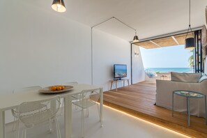 Ein modernes Wohnzimmer mit Holzboden, weißen Möbeln, einem Fernseher und Blick auf den Ozean.