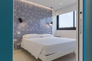 Ein modernes Schlafzimmer mit Wandverkleidung aus blauen und weißen Fliesen, einem weißen Bett und einem Fenster mit Blick.