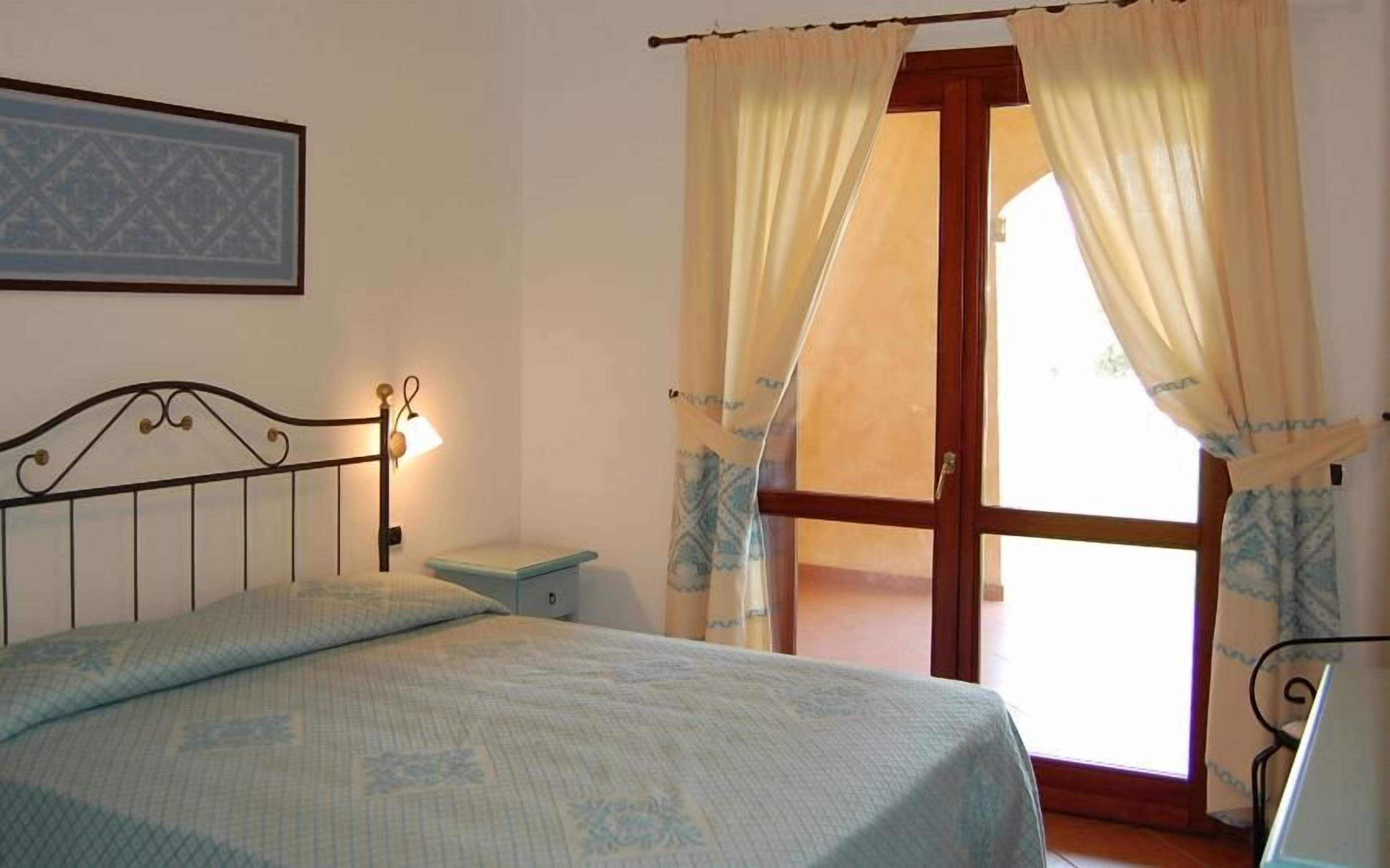 A bedroom with a bed, a nightstand, a lamp, and a window with curtains.