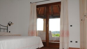 Een slaapkamer met een bed, een raam met gordijnen en uitzicht op groen.