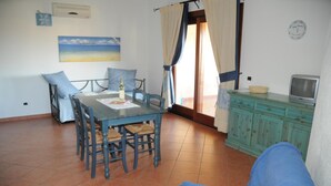 Un coin repas avec une table et des chaises, un canapé, un téléviseur posé sur un meuble et un tableau accroché au mur.