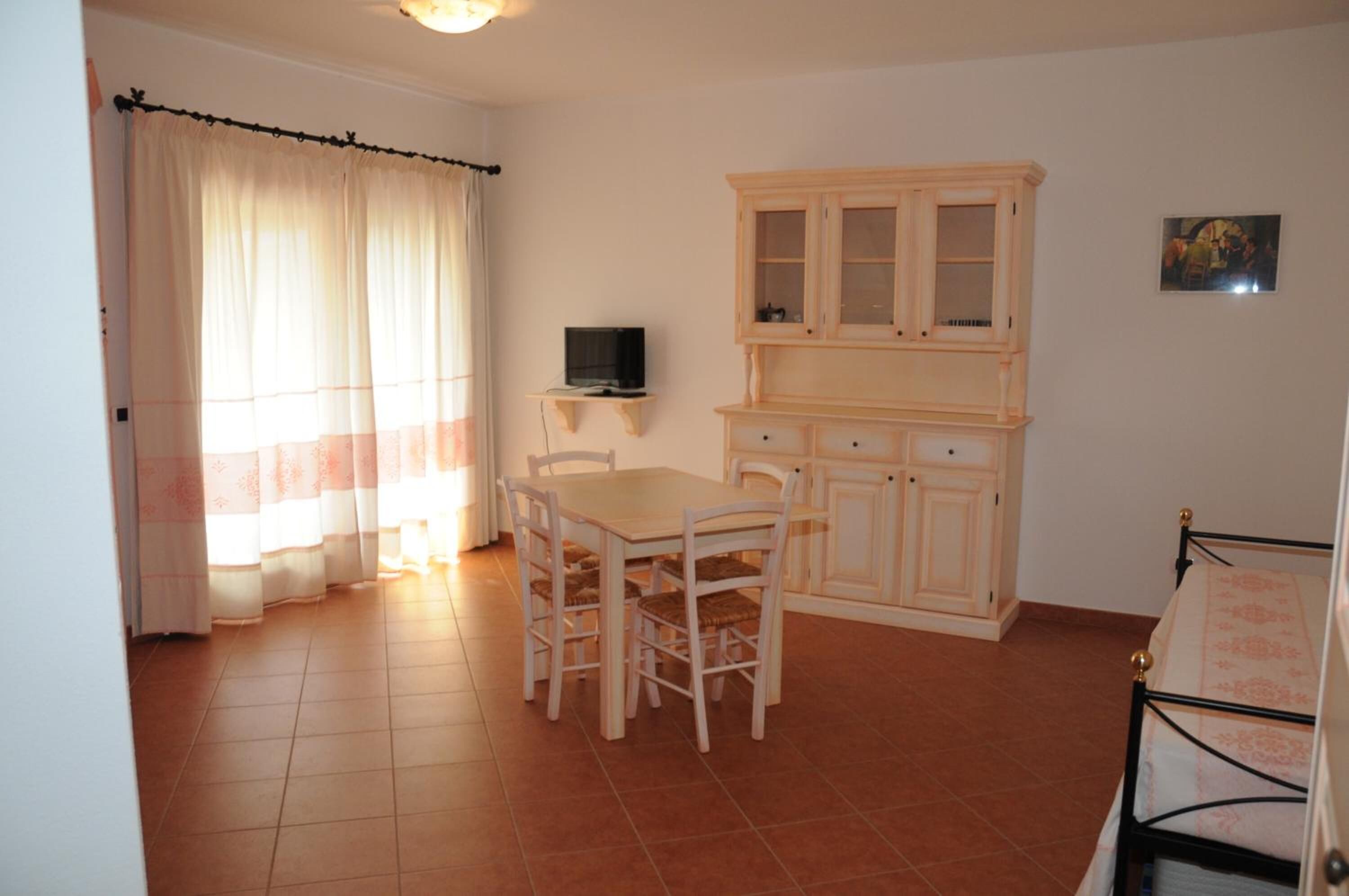 Um quarto com uma mesa de jantar, cadeiras, televisão, armário e cama.
